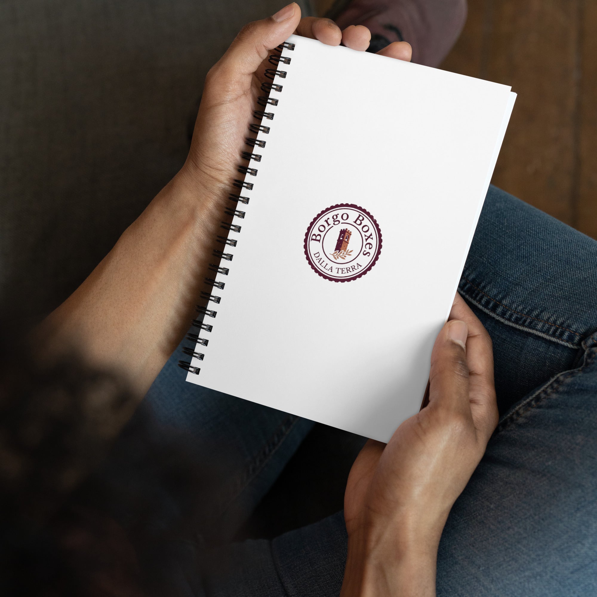 A man holds a spiral notebook with the Borgo Boxes logo as he dreams of italian gift baskets.